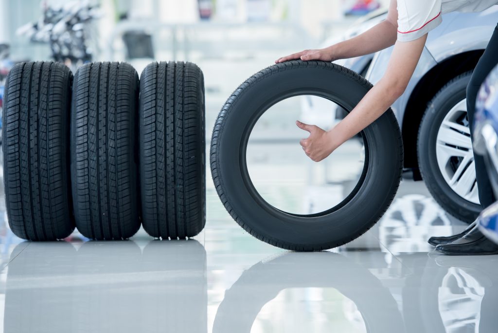 A person selecting a tire from a stack of tires in a showroom or auto shop, showcasing tire options for vehicles.