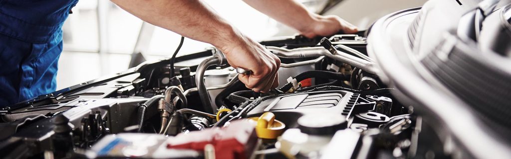 A mechanic working under the hood of a car, performing maintenance on the engine.
