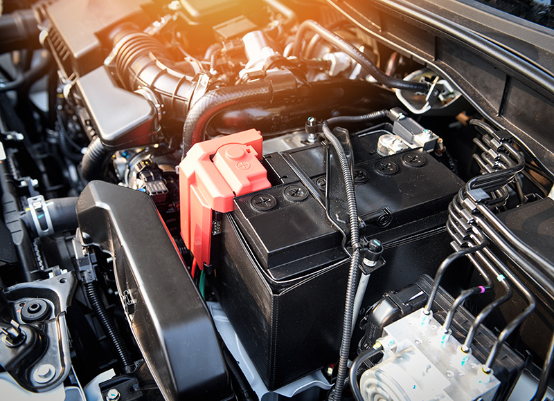 Car battery and engine bay components under the hood of a vehicle.