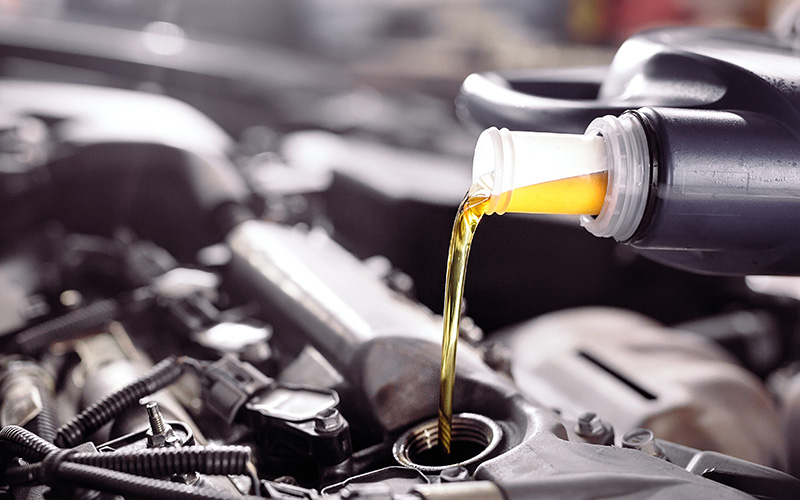 Motor oil being poured into a car engine during routine vehicle maintenance.