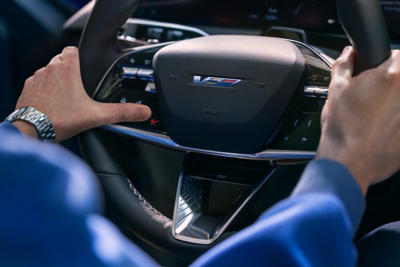 Close-up of a Man About to Press the V-Button on the 2026 OPTIQ-V Steering Wheel | Val Ward Cadillac in Fort Myers FL