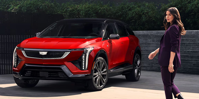 Red Cadillac OPTIQ electric SUV with a woman standing beside it.