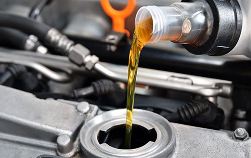 Motor oil pouring from a plastic bottle into an engine's oil filler.